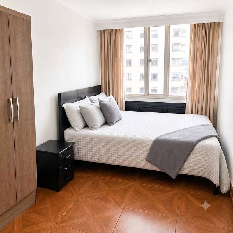 Habitación Comfort con clóset, mesa de noche, cortinas largas y vista a la ciudad.