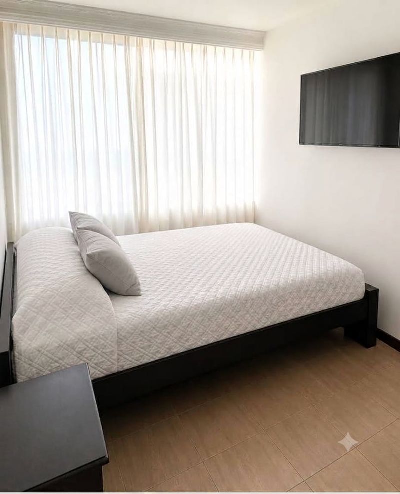 Comfort: cama con cortinas largas y televisor sobre consola.